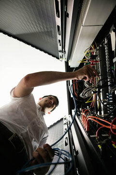 Adult male technician reaching into server rack and sorting colorful ethernet cables in data center