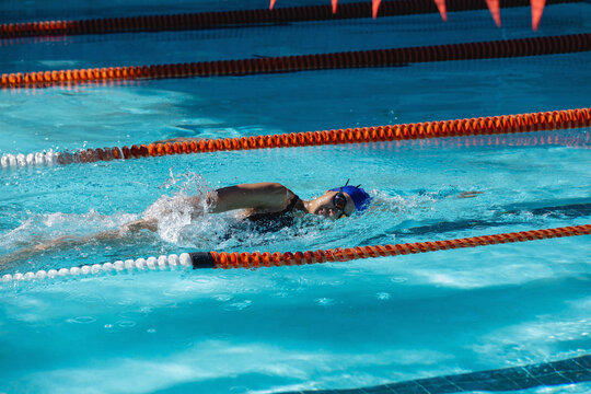 Female swimmer in swimsuit swimming front crawl in outdoor pool between orange lane dividers