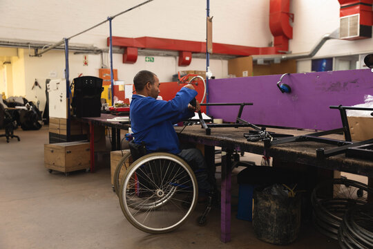 Man in wheelchair tightening metal frame with wrench at factory bench with partition, copy space