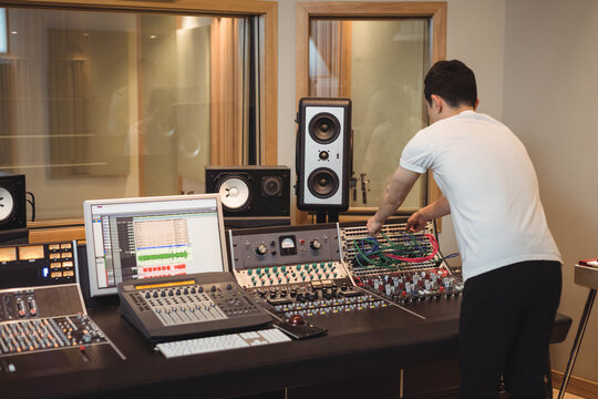 Asian man plugging colorful patch cables into mixing console bay in studio control room, copy space