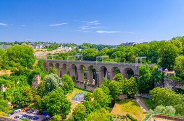 Pulvermuhl Viaduct Biisser Breck railway stone arch viaduct bridge across Alzette valley and Maierchen stone defensive wall in Luxembourg City centre, park with green trees and blue sky background