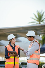 Two aviation engineers wearing safety helmets and reflective vests review maintenance data on digital tablets while inspecting an aircraft at an airport, highlighting teamwork, technology, and safety.