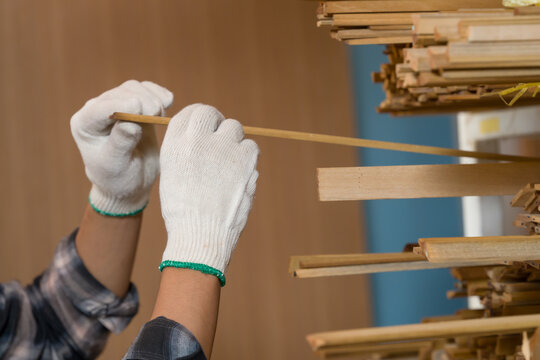 Close up view of gloved hands measuring thin wooden strip during material inspection process in woodworking shop, professional carpenter checking size accuracy for furniture manufacturing preparation - Powered by Adobe