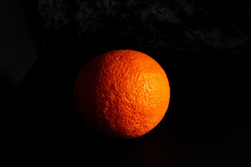 Fresh whole orange isolated on dark background with copy space. Studio still life with dramatic lighting, strong contrast and visible texture. Ideal for food, health and freshness concepts.