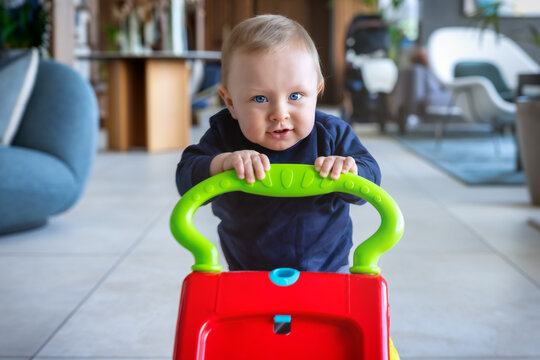 Portrait of a blonde baby boy pushing his walker toy and learning his first steps to walk<