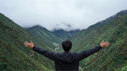 Man embracing the view in a lush green mountain valley with clouds, enjoying nature's beauty and tranquility