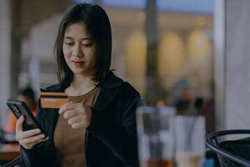Young asian woman using phone and credit card online shopping for ordering food, or buying something at cafe. Female person doing payment with mobile smartphone for business.
