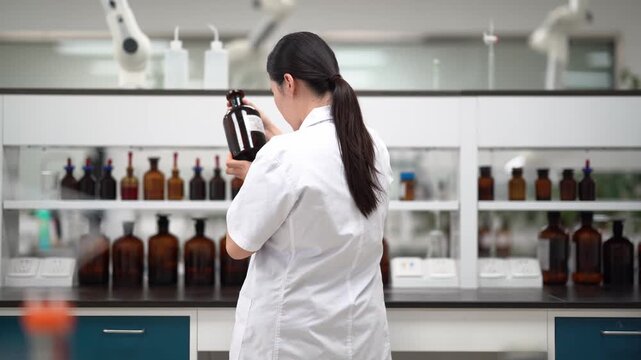 Female researcher in laboratory holding a reagent bottle and observing closely