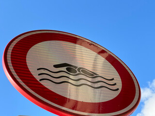 No swimming allowed sign against a clear blue sky with wispy clouds