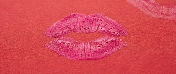 Pink lipstick kiss print on red textured paper background close up
