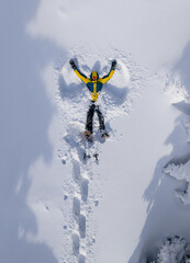 Young man making a snow angel while wearing snowshoes in fresh powder snow. Playful winter moment in a pristine snowy landscape, expressing joy, freedom, and connection with nature.