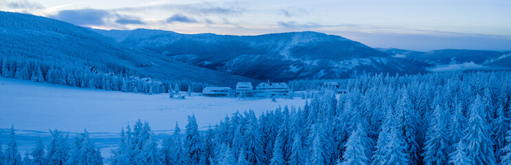 Winter landscape of the Krkono&scaron;e mountains in the Czech Republic with snow covered forests, mountain ridges, and alpine buildings. Calm blue hour atmosphere with pristine snow and rolling hills.