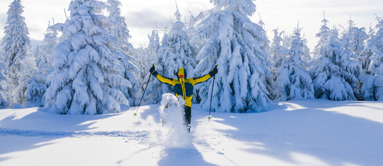 Happy young man celebrating in a snowy winter landscape while snowshoe hiking. Joyful moment in a frost covered forest, expressing freedom, energy, and connection with nature.