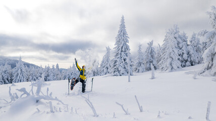 Happy young man celebrating in a snowy winter landscape while snowshoe hiking. Joyful moment in a frost covered forest, expressing freedom, energy, and connection with nature.
