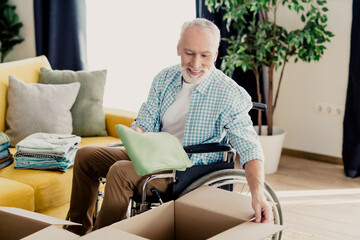 Kind elderly man in wheelchair packing box in a cozy living room, showcasing independence, family warmth, and inclusion