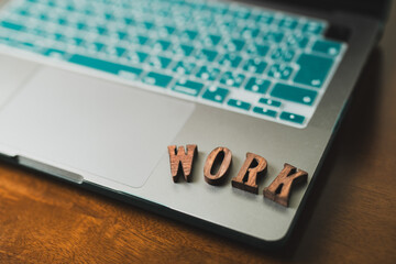 木のデスクに置かれたノートパソコンとWORKの文字
