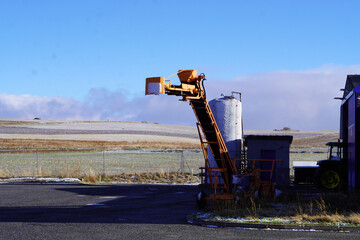 rural agricultural scene with a silo, a tractor, and a conveyor belt, with snow-covered fields in the background