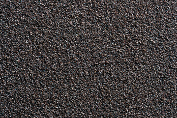 A high-resolution full-frame macro photograph of a dark, coarse, and grainy abrasive texture, resembling sandpaper or a rough stone surface. Ideal for construction, DIY, and industrial design concepts