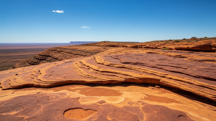 Australian rocky plateau showcasing flat stone formations and expansive desert landscape, sunlight casting shadows on layered rocks.