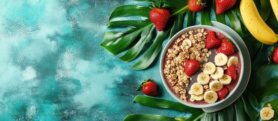 Vibrant Smoothie Bowl with Fresh Fruits, Granola, and Tropical Leaves on Textured Teal Background.