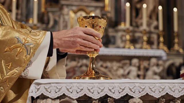 Priest performing consecration during mass, holding and placing a golden chalice on the altar for catholic ceremony.