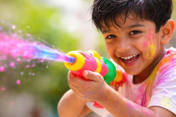 Joyful child celebrating holi with vibrant water gun and colorful paints outdoors
