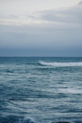 Moody vertical seascape with deep blue water and crashing waves, minimalist coastal background.