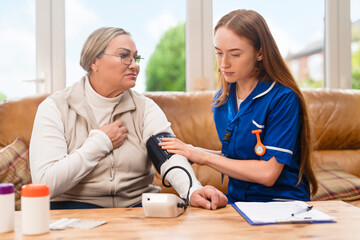 Nurse checks blood pressure of patient in home setting during afternoon visit