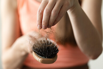 Woman takes off long loss hair from the hair brush. Closeup, selective focus.