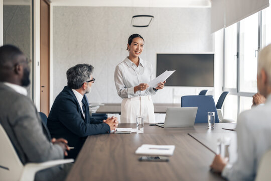 Asian businesswoman presenting to diverse team in office meeting - Powered by Adobe