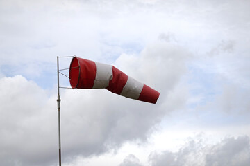 Red and white windsock indicating wind direction and speed approximate 6 knots against a cloudy sky on aerodrome airfield view close-up