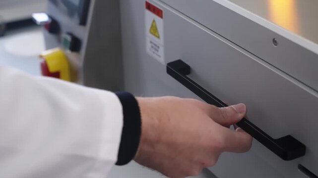 Silicon wafer secured in a metal dicing frame inside a precision semiconductor processing machine, with an operator adjusting the control panel and emergency stop on equipment