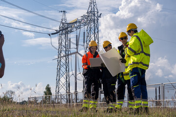 Workers examine plans near power lines during the day while wearing safety gear and hard hats