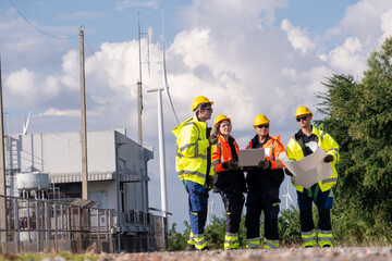Group of workers examine plans near wind turbines during daytime at a construction site
