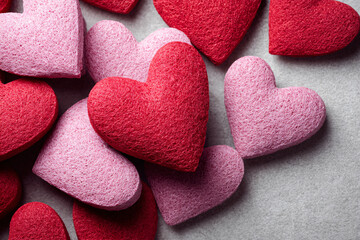 Obraz premium Close-up of textured red and pink hearts scattered on a grey background.