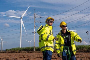 Two workers discuss tasks near wind turbines on a sunny day with blue sky in a rural area