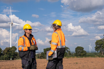 Fototapeta premium Workers discuss plans on a wind farm site in clear weather with wind turbines visible in the background during the afternoon