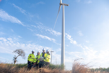 Team of workers stands near a wind turbine discussing project plans in a field during daytime under clear blue skies © Freeday photo