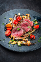 Fine dry aged beef filet steak rare tataki style cut tagliata with caramelized chicor&eacute;e, tomato and almonds served as close-up on a design plate