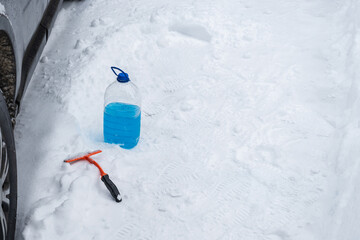 Winter car emergency setup with windshield washer fluid bottle and ice scraper on snow near...
