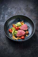 Fine dry aged beef filet steak rare tataki style cut tagliata with sliced zucchini, tomato and almonds served as close-up in a design bowl