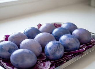 Purple and blue gradient Easter eggs arranged on a tray with red cabbage leaves for decoration. Holiday decoration for greeting card.