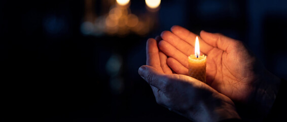 Hands holding a burning beeswax candle in the dark. Spiritual concept of hope, prayer and faith during Lent vigil. Religious background with warm bokeh lights and copy space.
