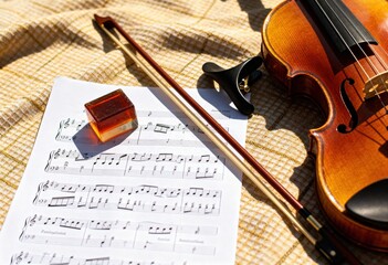 Naklejka premium Violin and sheet music on checkered blanket with rosin.