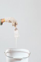 Painter holding a brush with white paint dripping into a bucket isolated.
