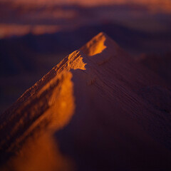 Dramatic orange sunset light illuminates the textured rocky peaks of a majestic mountain range under a deep purple twilight sky