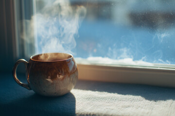 warm cup emitting steam, placed on a windowsill with a snowy background