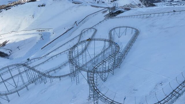Drone view of a bobsled mountain coaster winding through the snow-covered Caucasus mountains in Bakuriani resort, featuring people enjoying the winter attraction.
