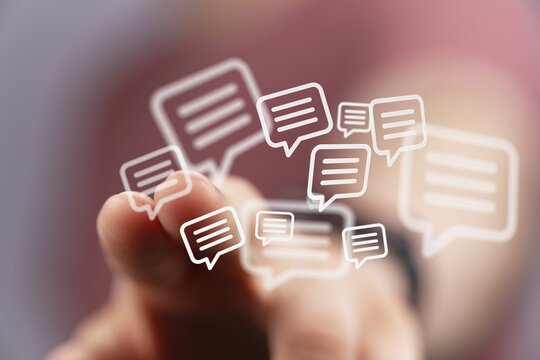 Close up of a hand interacting with a digital communication concept, featuring floating chat bubble icons, representing social media networking - Powered by Adobe