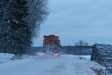 A truck with a load of logs is driving on a snowy road © talavietis